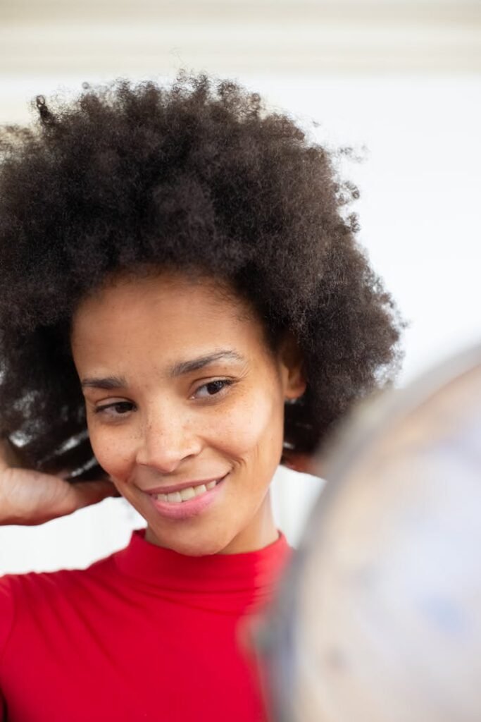 Bonjour tout le monde ! Portrait of a confident woman with afro hair, smiling as she adjusts her hairstyle, shot outdoors with natural lighting.